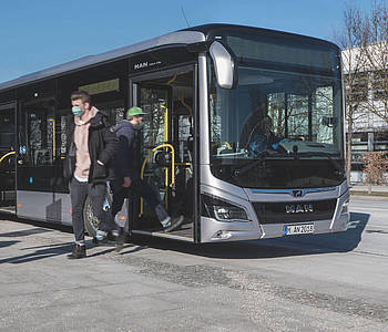 Menschen mit Masken steigen an einer Haltestelle aus einem Bus