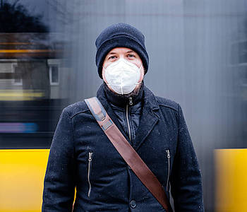 Mann mit FFP2-Maske steht vor einem fahrenden Bus