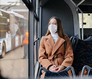 Frau mit Maske sitzt im Bus