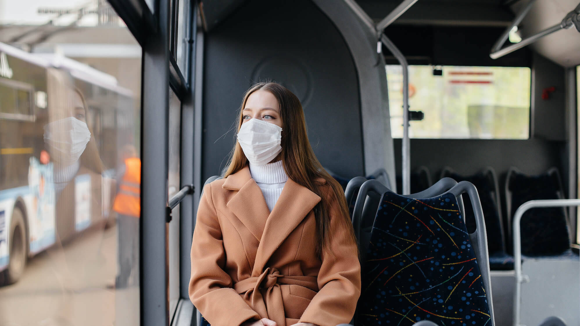 Frau mit Maske sitzt im Bus