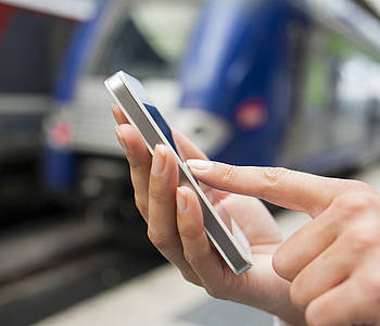 Frau bedient ihr Smartphone am Bahngleis