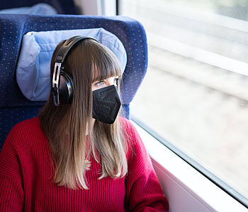 Frau sitzt mit Maske in der Bahn und hört Musik