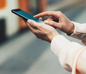 Frau steht mit ihrem Smartphone vor der Bahn.